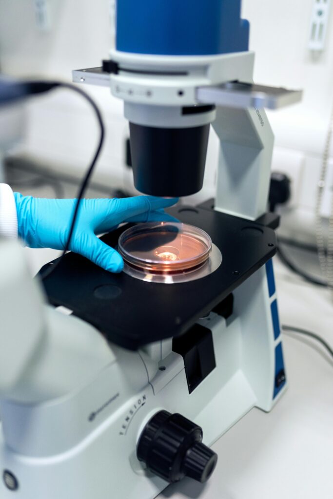 pexels-photo-3912365-3912365 Scientist using a microscope to examine petri dish samples in a laboratory setting.